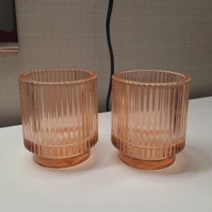 Räfflade glasljuslyktor från Mio - Två stilrena glasljuslyktor i en varm, rosa/orange ton med räfflad design. Perfekta för att skapa en mysig atmosfär i hemmet. Handdisk rekommenderas för att bevara kvaliteten. Skriv vid frågor!💓