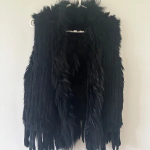 Svart pälsväst - Snygg svart pälsväst med långa, mjuka pälsdetaljer. Perfekt för att ge en lyxig touch till din outfit. Västen är ärmlös och har en öppen design framtill.
