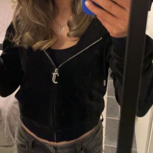 Svart velour hoodie från Juicy Couture - Snygg svart velour hoodie från Juicy Couture med dragkedja och glittrande detaljer. Den har en stor huva och fickor framtill. På baksidan finns texten 'Juicy' i glittriga bokstäver. Perfekt för en avslappnad och stilren look. Några rhinestones har blivit lite missfärgade på dragkedjan inget som märks så mycket dick. Alla stenar på ryggen sitter kvar😊