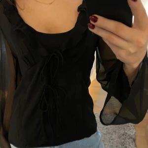 Svart volangblus i mesh - Superfin volangblus i mesh med knytning framtill. Perfekt festtopp! knappt använd