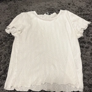 Vit blus från ONLY - Säljer en söt vit blus från ONLY i storlek XS. Blusen har korta ärmar med volangdetaljer och ett diskret mönster. Perfekt för en somrig look!