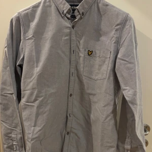 Ljusblå/grå skjorta från Lyle & Scott - Snygg skjorta från Lyle & Scott i M slim fit. Skjortan är i en ljusblå/grå nyans och har även bröstficka. 