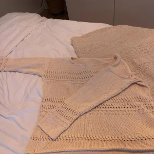 Beige stickad tröja - Säljer en mysig beige stickad tröja med dekorativa hålmönster. Tröjan har långa ärmar och en rund halsringning. Perfekt för kyliga dagar!
