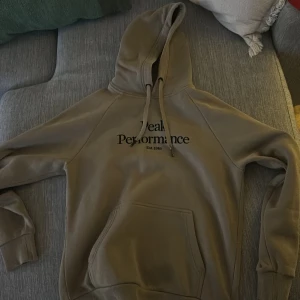 Beige hoodie från Peak Performance - Säljer en snygg beige hoodie från Peak Performance med tryck framtill. Den har en klassisk design med justerbar huva och en stor magficka. Perfekt för en avslappnad stil.