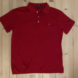 Röd pikétröja från Ralph Lauren - Säljer en snygg röd pikétröja från Ralph Lauren med klassisk krage och knappar. Tröjan har en broderad logotyp på bröstet och är i slim fit-modell. Perfekt för en stilren look.