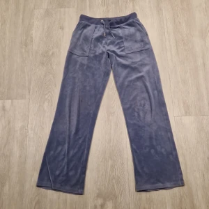 Blå mjukisbyxor ifrån juice coutore - Säljer ett par blå mjukisbyxor med breda ben och elastisk midja. Byxorna har praktiska fickor både fram och bak samt juicy coutore märket snyggt broderat på ena benet. Perfekta för en skön, snygg och avslappnad stil.