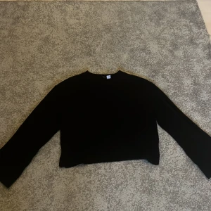 Svart croppad tröja - Säljer en stilren svart croppad tröja med långa ärmar. Perfekt för en avslappnad look. Tröjan är enkel och mångsidig, lätt att matcha med olika outfits.