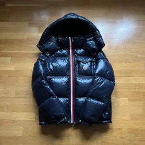 Mörkblå pufferjacka från Moncler - Snygg svart pufferjacka från Moncler med en iögonfallande röd och vit dragkedja. Jackan har en praktisk huva och en bröstficka med knapp. Perfekt för kyliga dagar.