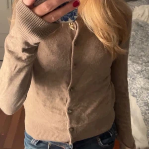Brun kofta från H&M - Snygg beige kofta med knappar framtill. Den har långa ärmar och ribbade muddar vid ärmslut och nederkant. Perfekt för en stilren look. Storlek xs men passar även mig som är har s. 