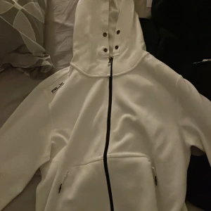 Vit hoodie från Ralph Lauren/ RLX - Säljer en stilren vit hoodie från Ralph Lauren med RLX-logga. Den har en dragkedja framtill och en praktisk huva  Perfekt för en avslappnad look.        Ny pris 3399kr