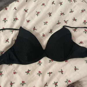 Svart bikiniöverdel med nätmönster - Snygg svart bikiniöverdel med vadderade kupor och ett coolt nätmönster på utsidan. Den har justerbara axelband för perfekt passform. Perfekt för en dag på stranden eller vid poolen. Helt ny och oanvänd i strl XL.