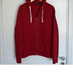 Röd hoodie från Polo Ralph Lauren - Säljer en snygg röd hoodie från Polo Ralph Lauren med dragkedja och justerbar huva. Den har en broderad logotyp på bröstet och långa ärmar. Perfekt för en avslappnad stil. Och den är dessutom tjock så man håller sig väldigt varm i den, hoodien är i bra skick. Har bara lite små rivmärken vid armarna och färgen är lite suddig.