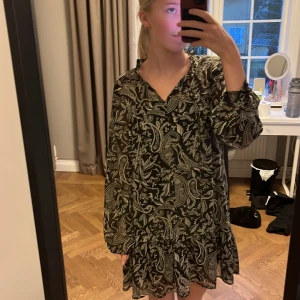 Svart och vit mönstrad klänning från Zara - Säljer en svart och vit mönstrad klänning från Zara med långa ärmar och volangdetaljer. Klänningen har ett paisleymönster och en lös passform, perfekt för en stilren look.