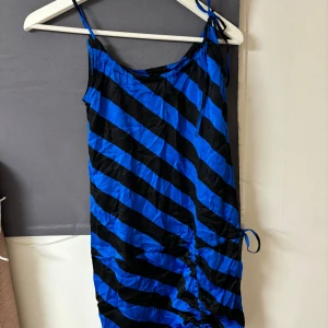 Blå och svart randig klänning från Twist & Tango - Snygg blå och svart randig klänning från Twist & Tango. Klänningen har smala axelband och en åtsittande passform. Perfekt för en trendig look!