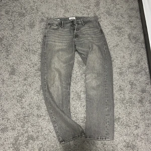 Grå jeans från Jack and jones - Snygga grå jeans från Jack and Jones med klassisk femficksdesign och knappgylf. Perfekta för en avslappnad stil. De har en rak passform och är tillverkade i slitstarkt denim.