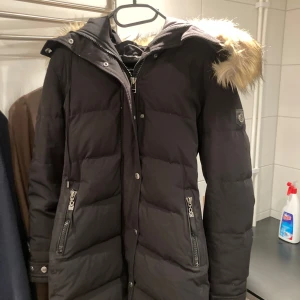 Svart vinterjacka från hollies modell subway - Snygg svart dunjacka med avtagbar huva och pälsdetalj. Jackan har dragkedja och knappar framtill samt praktiska fickor med dragkedja. Perfekt för kalla vinterdagar. Säljer pga att jag köpt ny o den är för liten för mig. Behövs nog tvättad de sista bilden 