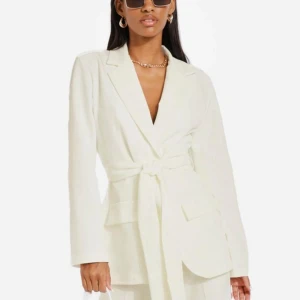 Vit kavaj med knytband - Elegant vit kavaj med knytband i midjan. Den har en klassisk design med långa ärmar och en stilren look. Perfekt för att ge en sofistikerad touch till din outfit.