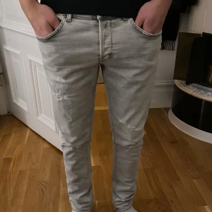 Ljusgrå jeans från Dondup  - Ljusgrå jeans från Dondup i storlek 34. Modellen är George skinny fit. Jeansen har designade tillgjorda hål på ena knäet och på lite andra ställen, men på knäet är det mest anmärkningsvärt. Jeansen är använda endast ett FÅTAL gånger!
