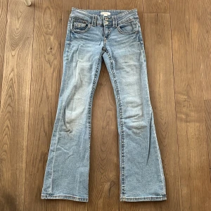 Blå bootcut jeans - Snygga blå bootcut jeans med klassisk femficksdesign och knappgylf. Perfekta för en avslappnad stil med en touch av retro. Passar bra till sneakers eller boots.