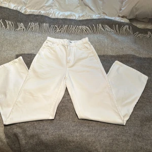 Vita wide leg byxor från Bershka - Snygga vita wide leg byxor från Bershka med dragkedja och knapp framtill. Perfekta för en stilren look. Byxorna har en hög midja och är tillverkade i ett bekvämt material.