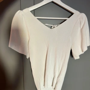 Vit topp - Säljer denna snygga topp, v-ringad bak o fram med gulligt knyte bak. 