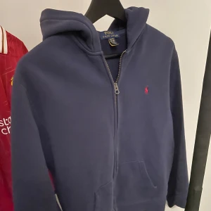 Mörkblå hoodie från Ralph Lauren - Säljer en snygg och bekväm mörkblå hoodie från Ralph Lauren. passar till både vardag och chill. den är i barnstorlek 18-20 vilket motsvarar XS-S