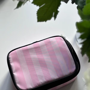 Rosa randig necessär från Victoria's Secret - Säljer en original superfin rosa randig necessär från Victoria's Secret. hely ny!!  perfekt för att förvara dina skönhetsprodukter. Necessären är i nyskick och har en stilren design med svarta detaljer. sista bilden ger en idé om hur stor väskan är! 
