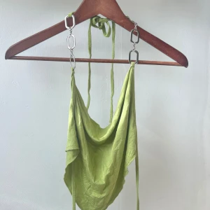 Grön axelbandslös topp med kedjedetaljer - Säljer en snygg grön axelbandslös topp med coola kedjedetaljer. Toppen har en draperad design och har öppen rygg. Använd 1 gång 