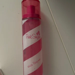 Pink Sugar Hair Perfume - Säljer en söt och fräsch hårparfym från Pink Sugar. Flaskan är randig i rosa och vitt, vilket ger en lekfull och ungdomlig känsla. Perfekt för att ge håret en extra doftboost och hålla det fräscht hela dagen. Flaskan är smal och lätt att ta med i väskan.