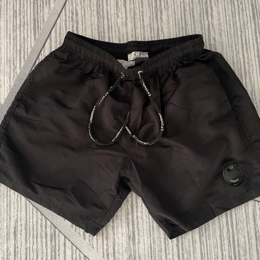 Säljer ett par snygga svarta shorts från C.P. Company. De har en elastisk midja med dragsko och ett coolt märke på benet. Perfekta för sommaren och riktigt bekväma med ett meshfoder inuti. Passar både till stranden och vardags!. Shorts.