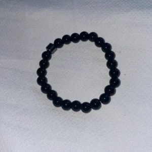 Svart pärlarmband - Snyggt svart armband med glansiga pärlor, perfekt för både vardag och fest. Armbandet är elastiskt och passar de flesta handleder. Enkelt men stilrent, det ger en elegant touch till vilken outfit som helst.