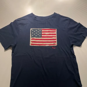 Ralph lauren t-shirt - Säljer denna fina Ralph lauren t shirten i barnstorlek som sitter som XS/S. Slitningarna på flaggan är original och tröjan är i perfekt skick. Hör av dig vid fler fler frågor!