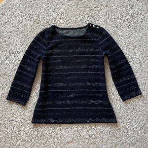 Trekvartsärmad tröja - Säljer en blå och grå randig tröja med trekvartsärm. Den har knappar vid axeln för en extra detalj. Perfekt för både vardag och lite finare tillfällen. 