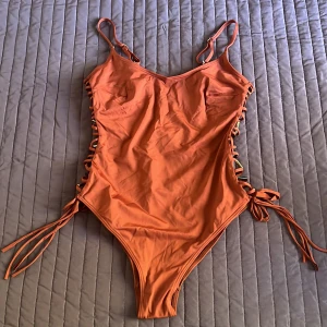 Orange baddräkt från H&M - Säljer en superfin orange baddräkt/body  från H&M i storlek S. Den har snygga snörningsdetaljer på sidorna som ger en cool look och justerbara axelband för perfekt passform. Perfekt för sommarens alla badäventyr! 🧡använd som body med högmidjade byxor
