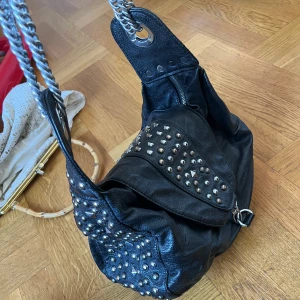 Rockig rock metal punk väska med nitar - Slitning på baksida enligt bild. Syns inte när den används då den sidan ligger mot kroppen.
