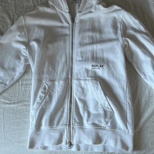 Replay hoodie - Säljer en stilren vit hoodie från Replay med dragkedja och känguruficka. Den har en liten logotyp på bröstet och är perfekt för en avslappnad look. Huvan ger extra komfort och stil. Skick 9/10 sjukt fet nu till våren/sommaren. Kontakta mig om du har några frågor//Maximilian😁