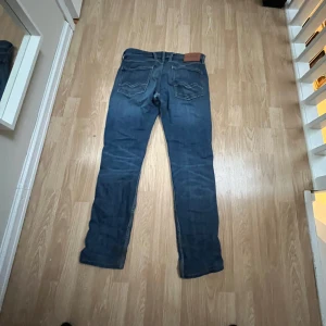 Blå jeans från Replay - Snygga blå jeans från Replay med klassisk femficksdesign och en läderpatch med logga på baksidan. Jeansen har en normal passform och är perfekta för en avslappnad stil. De har en knappgylf och subtila slitningar för en trendig look.