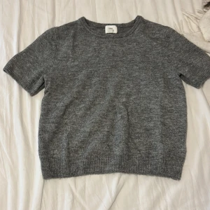 Mjuk grå stickad tröja från H&M - Säljer en stilren grå stickad tröja från H&M. Tröjan har korta ärmar och en rund halsringning, perfekt för lager på lager under kyligare dagar. Den är mjuk och bekväm, vilket gör den till ett mångsidigt tillskott i garderoben. Passar bra till både jeans och kjol. Den sticks ej.