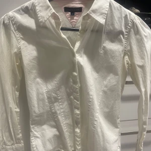 Vit skjorta från Tommy Hilfiger - Säljer en stilren vit skjorta från Tommy Hilfiger med klassisk krage och knappar framtill. Skjortan har långa ärmar och ett diskret broderat märke på bröstet. Perfekt för en elegant look. Passar XS 