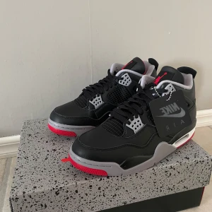 Nike Air Jordan 4 Retro - Snygga Nike Air Jordan 4 Retro sneakers i svart och grått med röda detaljer. Skorna har en klassisk design med snörning och en bekväm sula. Perfekta för dig som älskar stil och komfort.