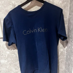  Calvin Klein T-shirt  - Snygg blå t-shirt från Calvin Klein med logga på bröstet. Perfekt för en avslappnad stil. Kortärmad och i mjukt material.