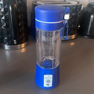 Bärbar blå mixer - Praktisk bärbar mixer i blått med genomskinlig behållare. Perfekt för smoothies och shakes på språng. Utrustad med en startknapp och en bärrem för enkel transport.
