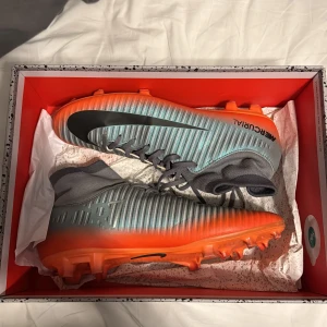 Nike Mercurial fotbollsskor - Snygga Nike Mercurial fotbollsskor i en cool kombination av grått och orange. Tar med ett par benskydd med dom. Skriv nåt prisförslag 