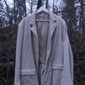 Beige manchesterkavaj - Säljer en stilren beige kavaj i manchester med knappar framtill. Kavajen har långa ärmar och två stora fickor. Perfekt för en avslappnad men ändå elegant look. En defekt är att på ena sidan är av ärmen är en av knapparna halvt av Ingen storleks etikett men passar som L.