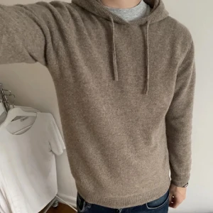 Beige merinoulls hoodie - Säljer en stilren beige merinoulls hoodie. Den har en mjuk och bekväm känsla med långa ärmar och justerbar huva med snören. Perfekt för kyligare dagar. Storlek M 