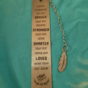 Metallbokmärke med inspirerande citat - Snyggt metallbokmärke med ett inspirerande citat ingraverat. Bokmärket har en kedja med en fjäderformad hängare. Perfekt för att hålla koll på var du är i din bok och få en daglig dos av motivation.