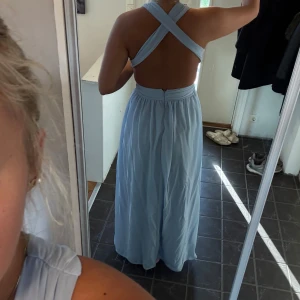 Ljusblå långklänning med öppen rygg - Elegant ljusblå långklänning med en v-ringad framsida och korsade band i ryggen som skapar en öppen rygg. Perfekt för sommarens festligheter. Storleken varierar lite från person till person men jag är en storlek 38 i midjan och den passar bra. Ny pris 1.600