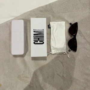 Svarta solglasögon från Chimi - Snygga bruna solglasögon från Chimi med en elegant cat-eye design. Perfekta för att ge din stil en trendig touch. Kommer med ett vitt fodral och en tygpåse för förvaring.