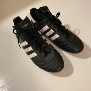 Adidas Copa Mundial fotbollsskor - Klassiska Adidas Copa Mundial fotbollsskor i svart och vitt. Skorna har snörning och är tillverkade i skinn. Perfekta för fotbollsentusiaster! Dessa fotbollsskor bärs ofta av fotbollsdomare runt om i hela världen. Storleken är 38 2/3
