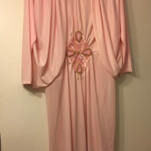 Rosa långklänning med pärldetaljer storlek S/M - Elegant rosa långklänning med unika pärldetaljer och paljetter i midjan. Klänningen har långa ärmar och ett draperat fall som ger en vacker siluett. Perfekt för speciella tillfällen.